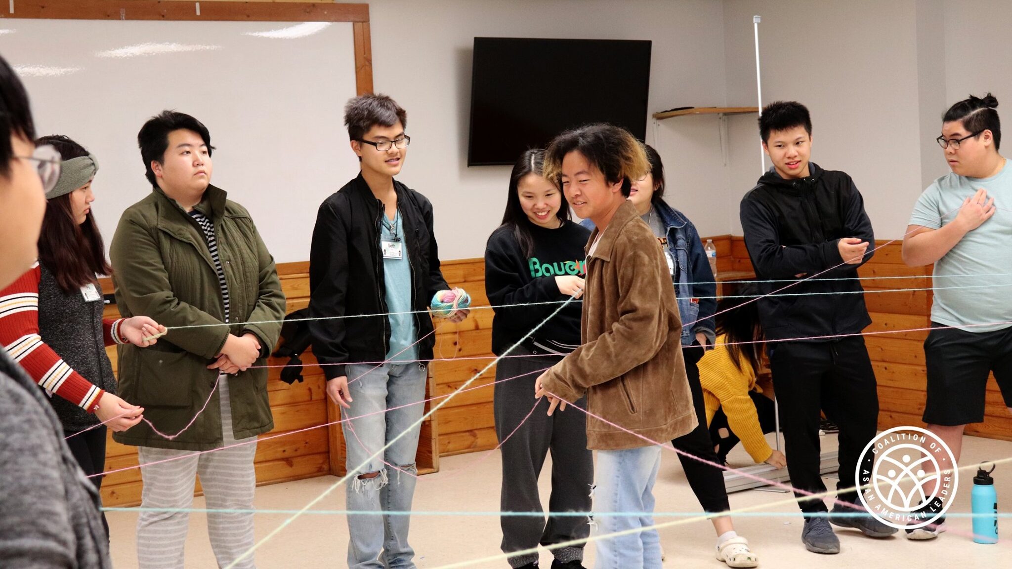 Nine youth stand in a circle holding strings at a Coalition of Asian American Leaders event