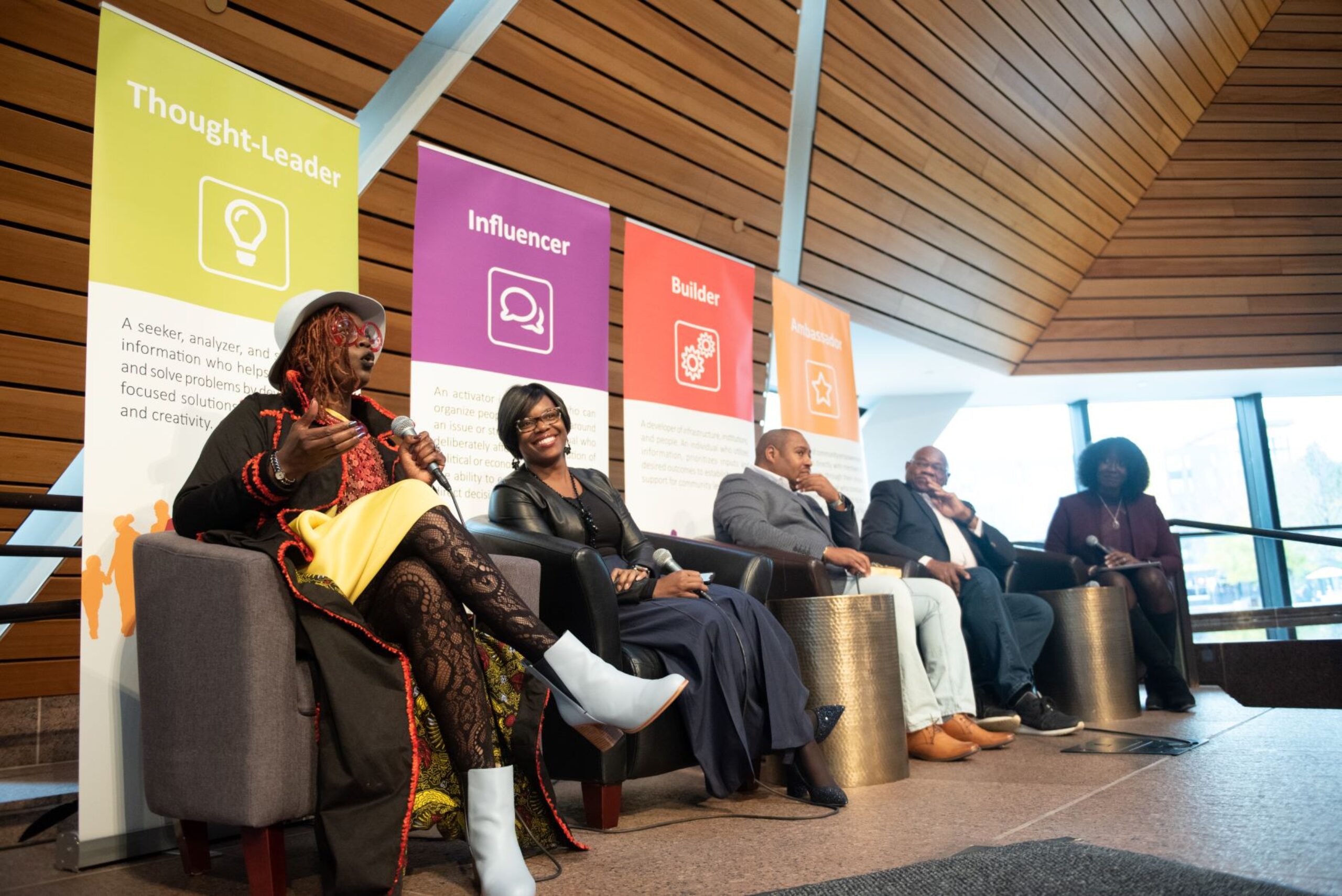 Five adults seated on a stage for an African American Leadership Forum panel. One speaks on a microphone