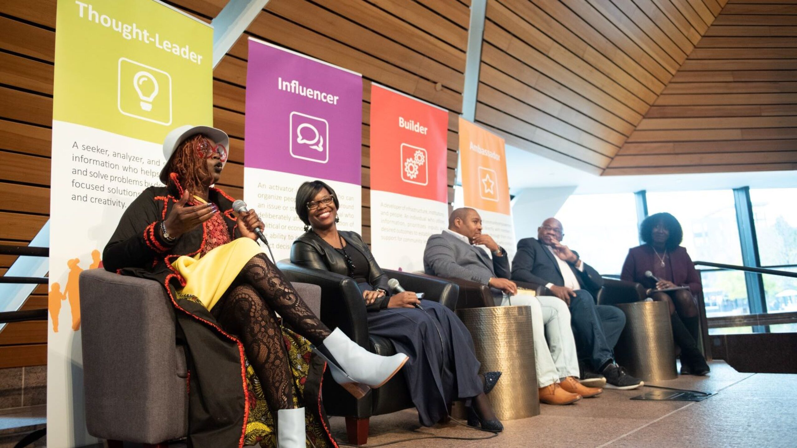Five adults seated on a stage for an African American Leadership Forum panel. One speaks on a microphone