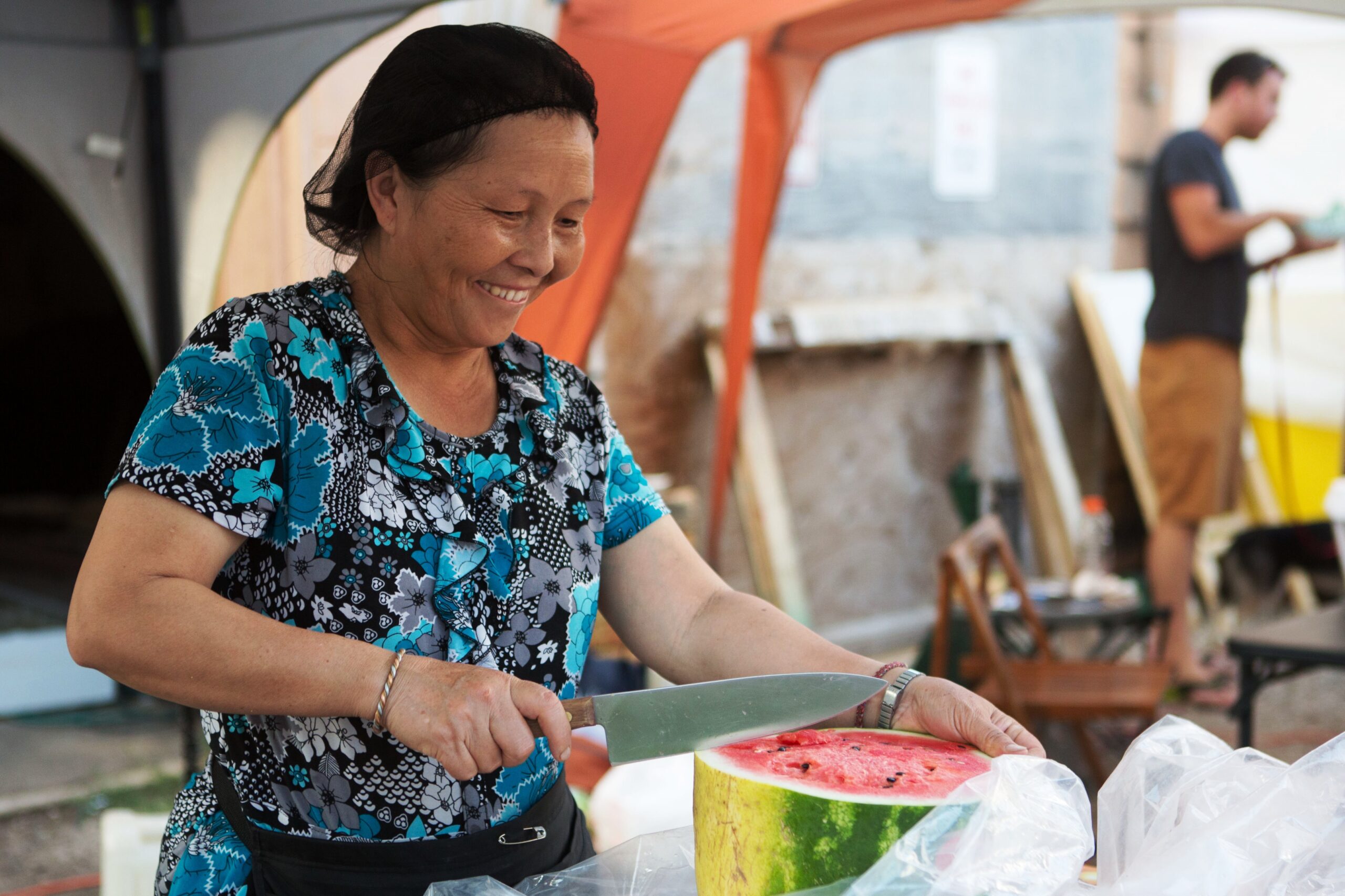 Person uses knife to slice watermelon in outdoor setting