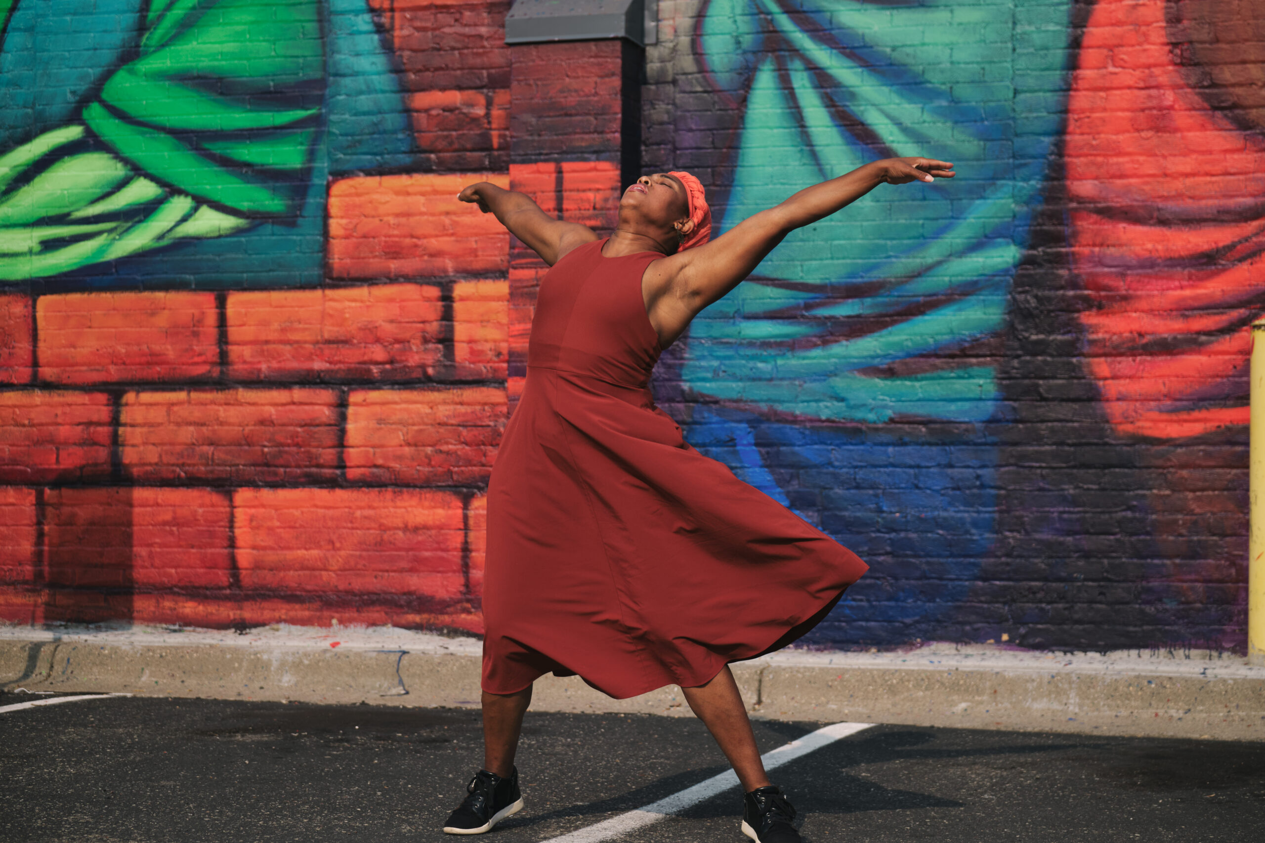 Brownbody Founder and Artistic Director Deneane Richburg dances with arms spread in front of mural