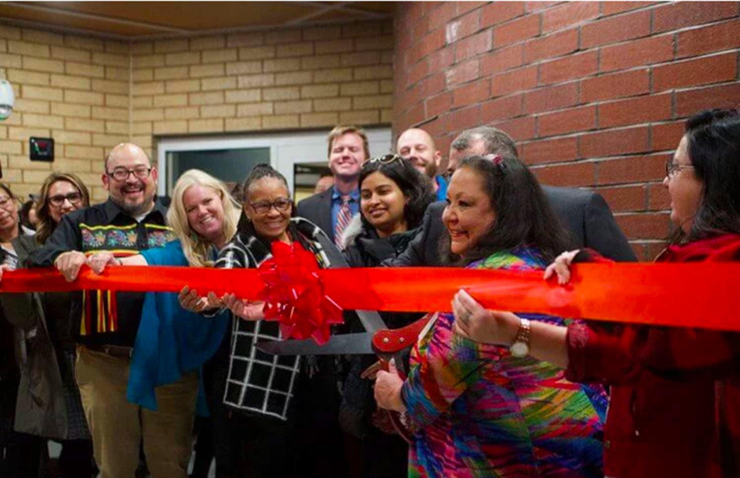 Large group of smiling people about to cut a large red ribbon at Mino Oski Ain Dah Yung supportive housing grand opening